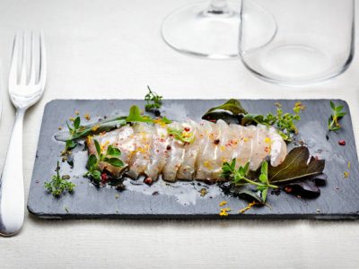 Carpaccio di orata marinata agli agrumi e erbette, olio arancio e mandorle.